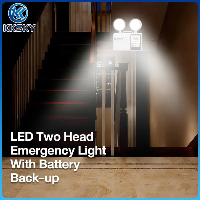 KKSKY LED two-head emergency light with battery backup shown mounted on a staircase landing in a real interior environment, with bright beams of light projecting outward. The product itself is white and mounted above the stairs.